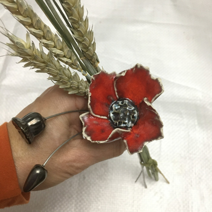 small red ceramic poppy ornament arrangement with corn held in a hand