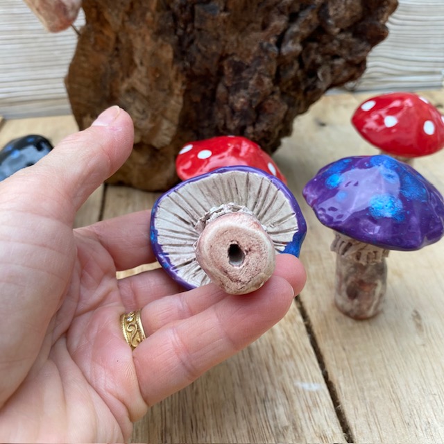 hand holding a ceramic fungi, showing the hole under the stem where a wire can be fitted