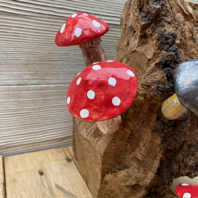 ceramic red and white spotted fungi displayed on a piece of decorative wood