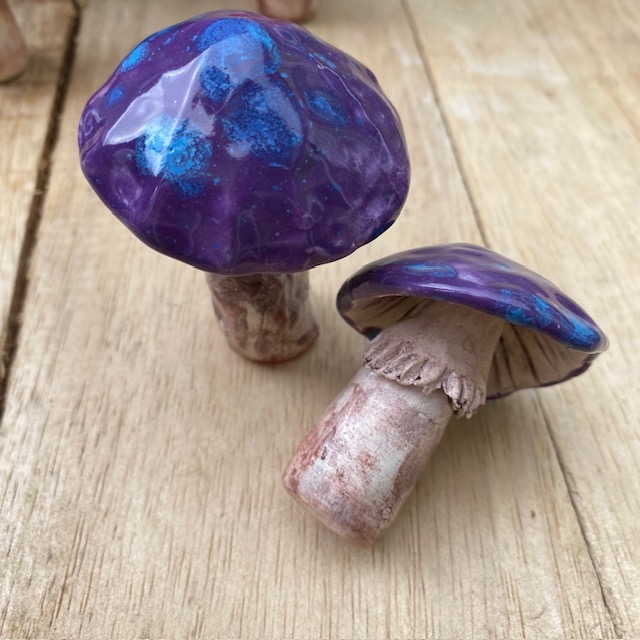 2 purple and blue spotted cap ceramic mushroom, one on its side to show stem details